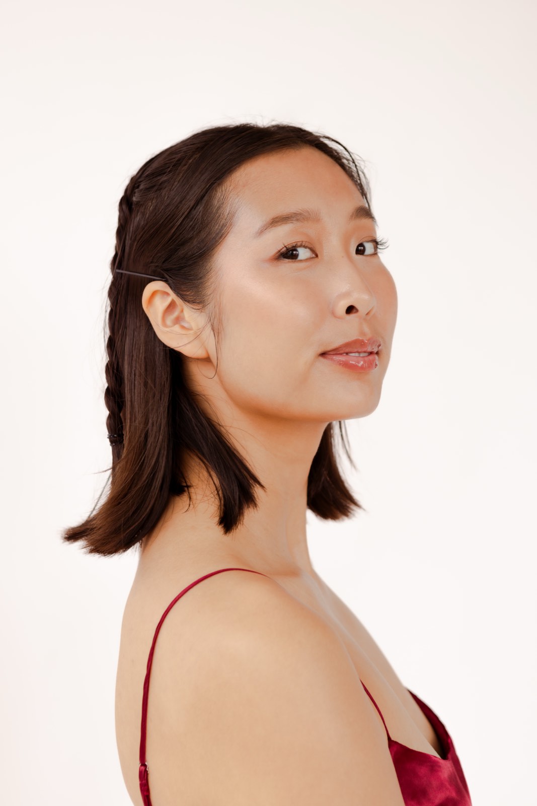 Profile portrait of Nikki glancing over her shoulder, hair in a half braid, wearing a deep red satin slip dress