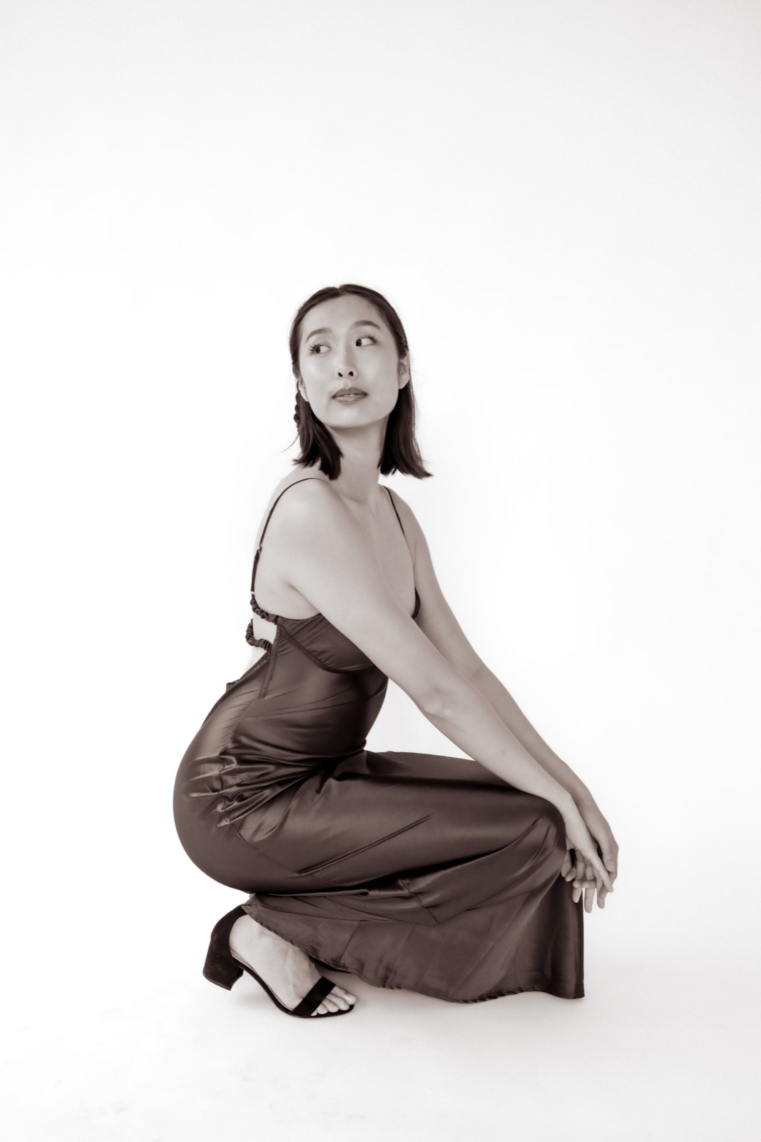 Sepia-toned photo of Nikki crouching in a long satin slip dress, looking back over her shoulder