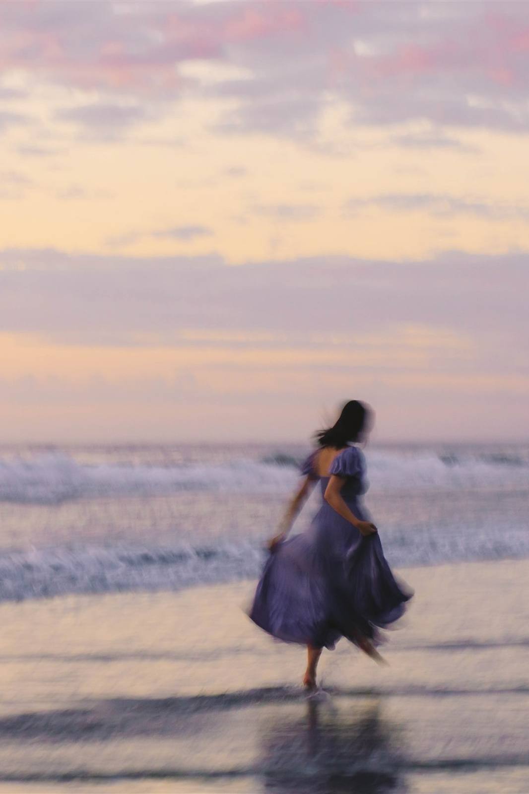 Nikki caught in motion blur walking across wet sand in a lavender dress, under a soft pink sunset sky
