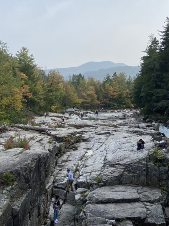 A wide granite river gorge framed by orange and gold autumn foliage in the White Mountains